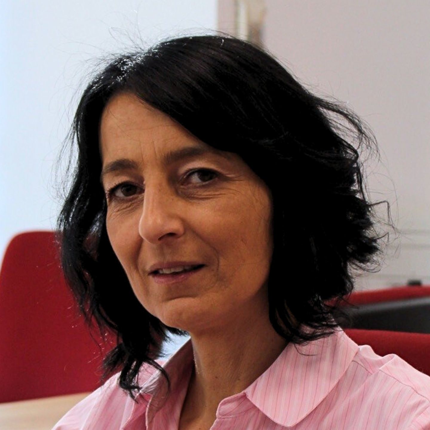 Cristina Pasere, directora de soporte de operaciones de cumplimiento normativo de EOS en Rumanía, está sentada en su escritorio con una blusa de rayas rosa y mirando a la cámara.