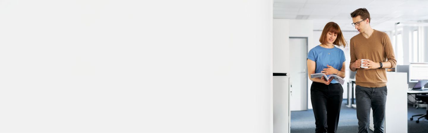 Dos colegas discutiendo en una oficina moderna cómo EOS puede proteger a las empresas de impagos y maximizar su liquidez en la gestión de cuentas por cobrar, mientras otro empleado trabaja en la computadora en el fondo.