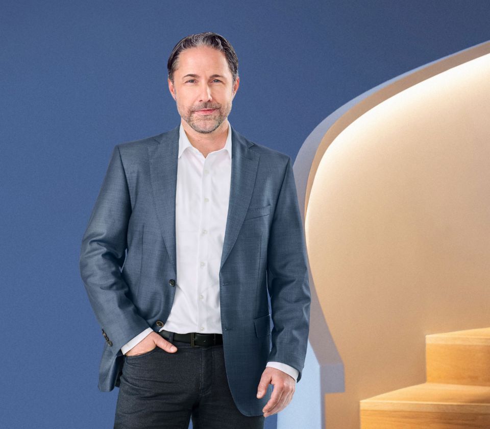 Marwin Ramcke, CEO del Grupo EOS, posa de pie frente a un fondo azul, vestido con una chaqueta oscura. Mira directamente a la cámara.