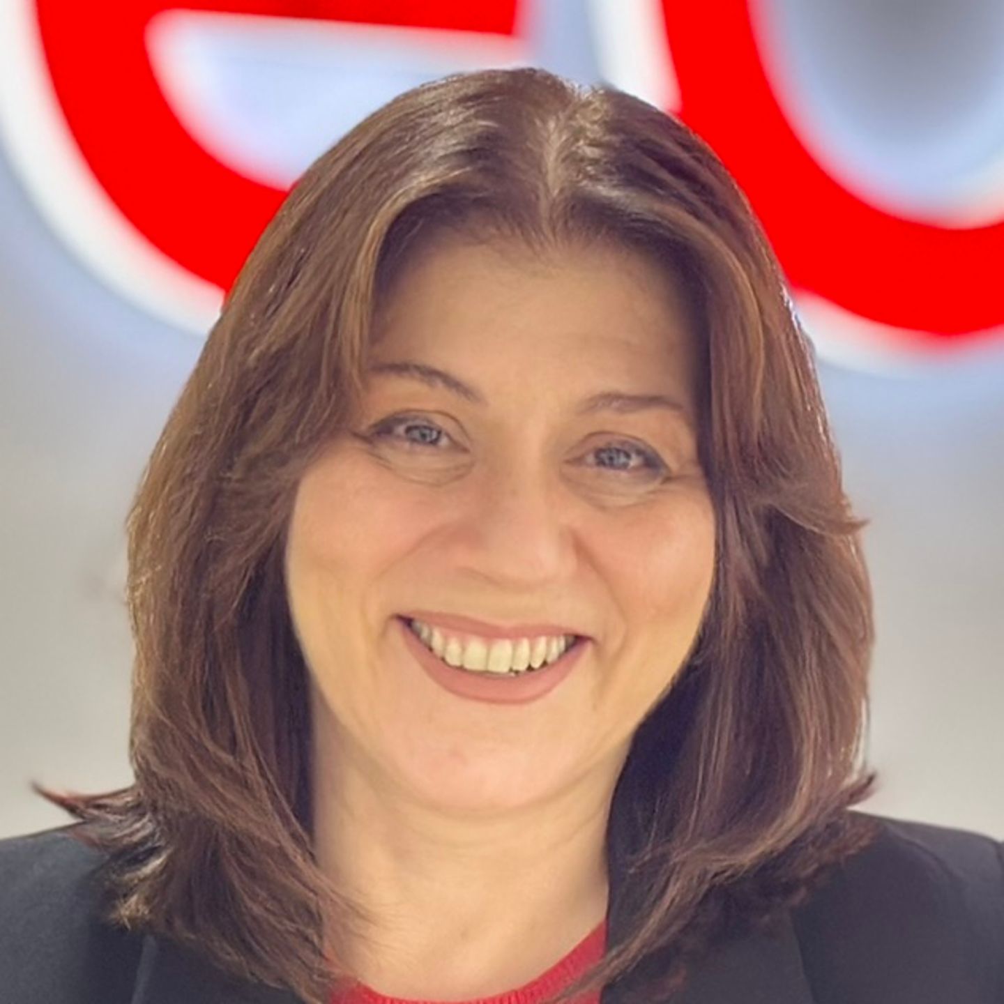 Belén Barreiro, agente del centro de contacto de EOS en España, está apoyada en un mostrador con una chaqueta negra y delante de un logotipo brillante de EOS.