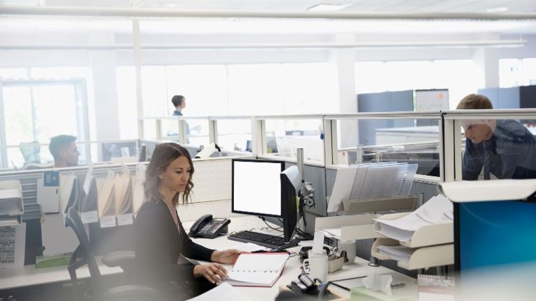 Digitalización: Tres empleados están en una oficina colectiva, una mujer está sentada entre papeles y su ordenador