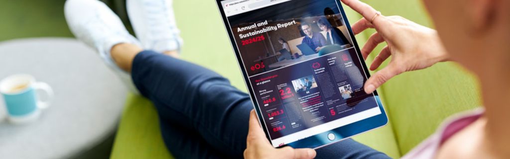 Persona en un sofá verde visualizando el Informe Anual y de Sostenibilidad de EOS 2024/25 en una tableta