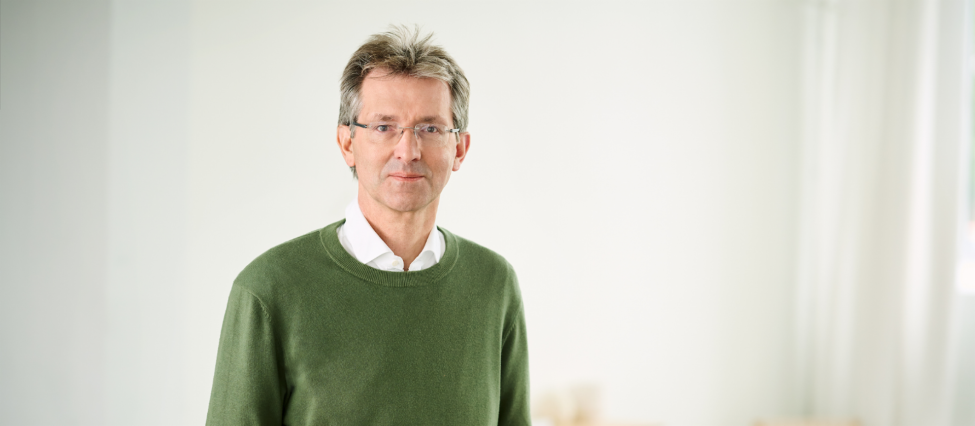 Justus Hecking-Veltman, CFO con un jersey verde bosque y una camisa blanca de pie en una estancia luminosa.