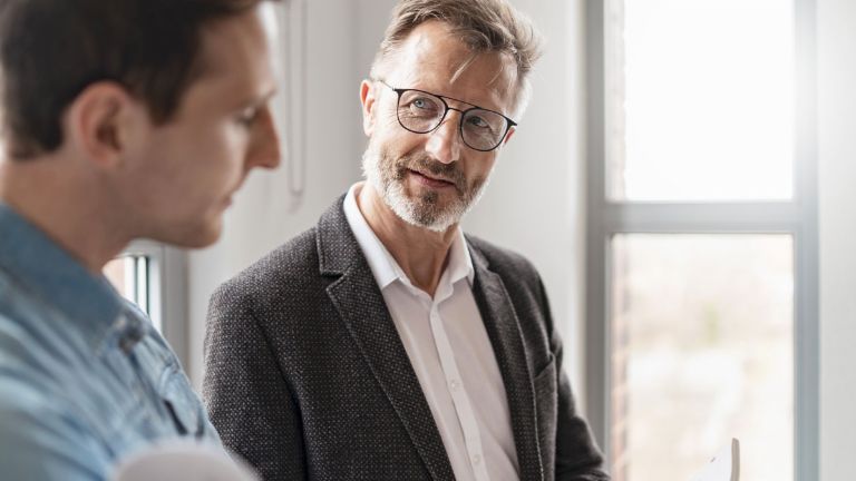 Dos hombres en una oficina discuten los resultados del estudio "Prácticas de Pago Europeas 2025" del Grupo EOS sobre la digitalización en la gestión de cobros.