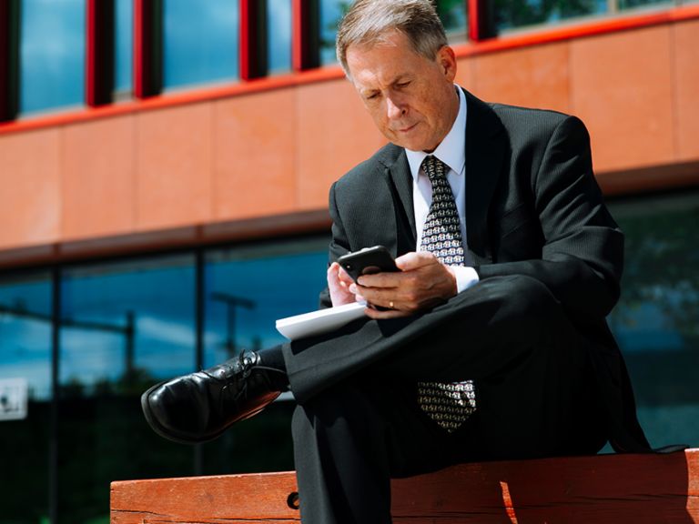 Raymond Pappot está sentado en un banco mirando su smartphone.